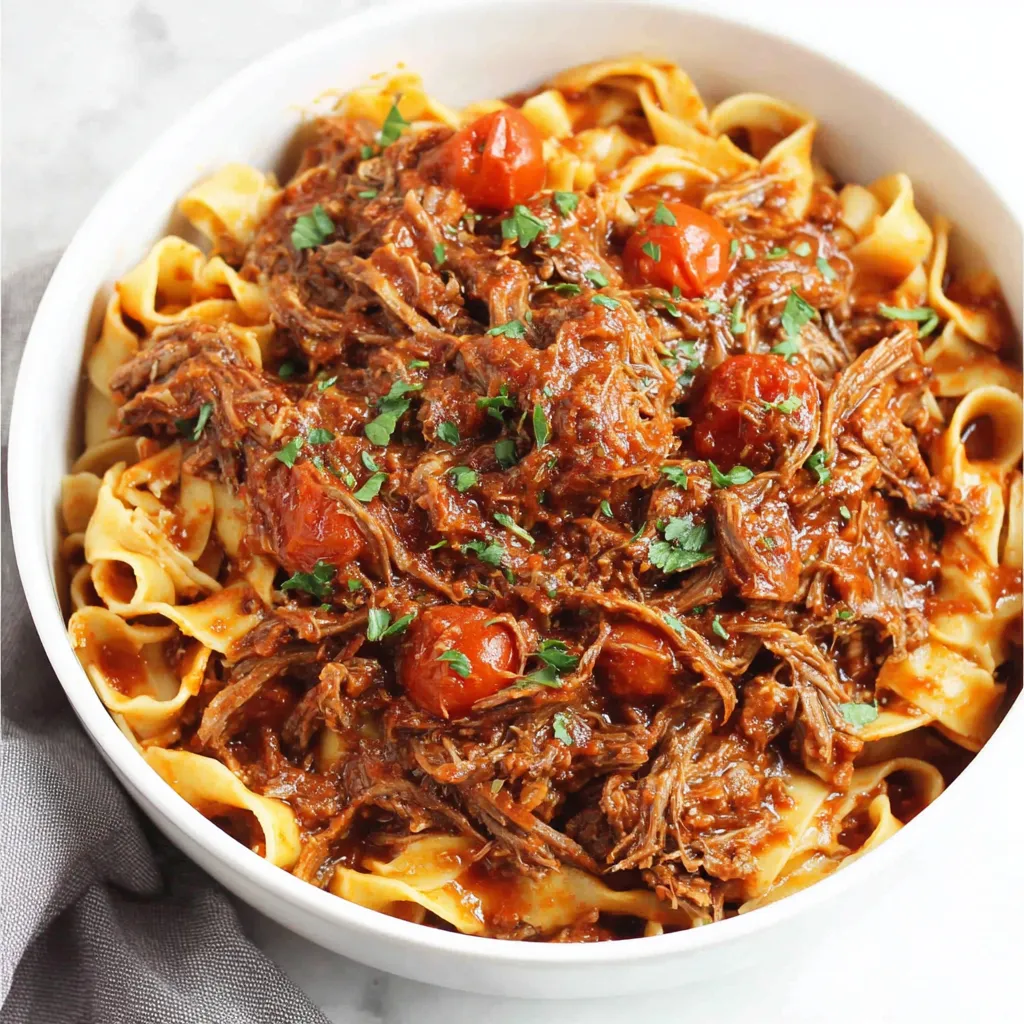 Easy Sunday slow cooker beef ragu simmers to perfection in a red sauce, creating a comforting and flavorful meal.