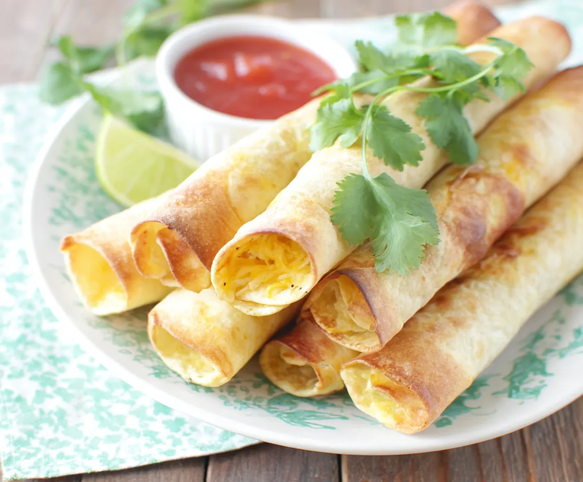 A close-up shot displays the crispy, golden-brown Baked Cream Cheese Chicken Taquitos fresh from the oven.