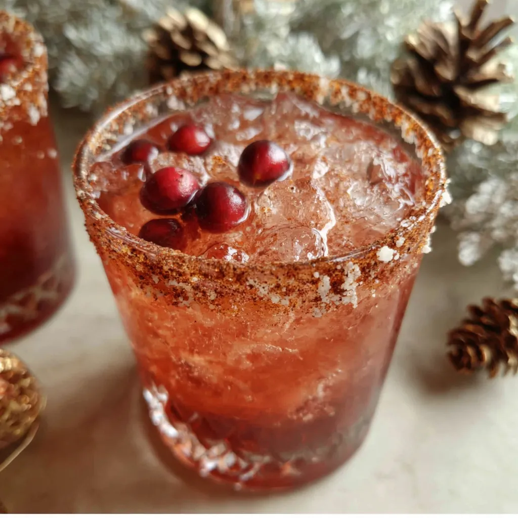 A festive Spiced Christmas Margarita cocktail is garnished with cinnamon sticks and cranberries for a holiday celebration.