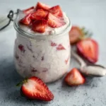 Strawberries and Cream Overnight Oats are beautifully layered in a glass jar, showcasing a delicious and healthy breakfast option.